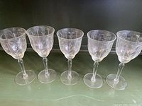Set of five vintage clear glass wine glasses with floral etching viewed side by side on table.