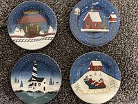 Top view photo of four ceramic Christmas plates, each showing unique holiday scenes in multicolor with red, blue, white, and green accents and snowy night background