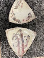 Two triangular ceramic platters with fish illustrations seen from above on a carpet, showing earth tone colors and minor surface wear.