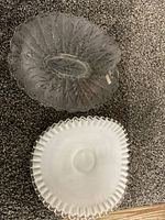 Two vintage Fenton glass plates on carpeted floor, one clear with leaf pattern and one white milk glass with ruffled edge