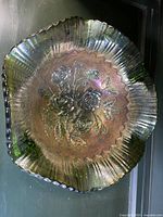 Top down view of vintage green glass bowl showing embossed floral rose pattern with iridescent sheen and scalloped edges.
