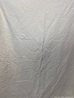 White bedspread hanging, showing textured floral pattern and wrinkles