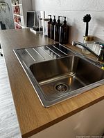 Close-up of wood-look laminate countertop and stainless steel sink with drying area and faucet, showing surface texture and finish