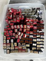 Overhead view of plastic bin containing numerous small boxes of Wella hair color tubes showing various red, blonde, brown shade boxes