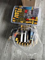 Plastic tub filled with yellow-labeled Wella Koleston Perfect boxes and a tied plastic bag of additional tubes on floor.