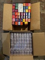 Two cardboard boxes: top contains assorted Colour Charm tubes in various bright shades, bottom contains uniform silver Wella Illumina tubes