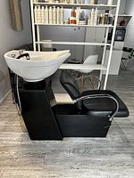 Side view of shampoo station showing white ceramic bowl, black vinyl chair, and black base