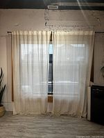 Curtain panels hung side by side on window with light filtering through, showing texture and length to floor.