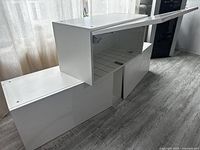 Three white high gloss wall cabinets assembled, placed on floor. All have upward opening doors with soft-close hydraulic hinges.