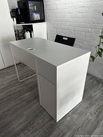 Side view of white desk showing integrated pull-out drawers and cabinet structure, with a cable management hole on top.