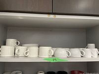 White coffee, espresso, and cappuccino mugs arranged on a shelf with matching white plates.