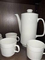 Photo showing white ribbed tall teapot with lid and several cups