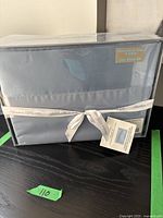 Packaged microfiber twin sheet set in blue with satin hem, wrapped with a ribbon stating 'Bordure 100% satin'.