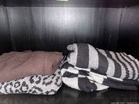 Four folded cashmere sweaters displayed on a black shelf showing colors and patterns: solid brown, grey leopard print, and black and grey stripes.