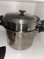 Stainless steel cooking pot with lid and black handles shown closed.