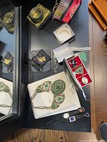 Photo showing a large green decorative necklace on white jewelry holder, two watches with black bands, and gold-tone earrings in black pouches