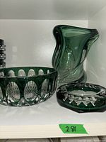 Three green crystal pieces on white shelf: bowl, ashtray, vase