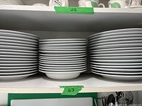 Three stacks of white porcelain plates (shallow bowls, salad and dinner plates) on shelf