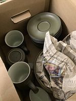 Top view of box with stacked plates, teacups, and partially wrapped items