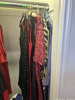 Photo showing six women's dresses hanging in a closet, displaying various colors and materials including sequins, lace, satin, and stripes.