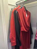 Four women's clothing items hanging on a closet rod: red dress, red shirt, black blazer, grey blazer.