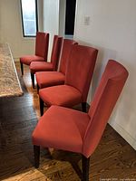 Five red microfiber dining chairs arranged in a row next to a granite countertop, showing their shape and upholstery.