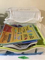 Clear plastic container with lid holding several stacked dish racks and paper flyers on top.