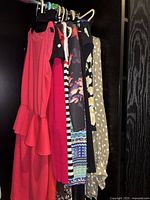 Six ladies dresses hanging in a closet showing various colors and patterns including coral, red, black, floral, stripes, and polka dots.