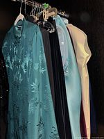 Seven assorted ladies dresses hanging on a rod, showing a variety of colors and fabric types including satin, velvet, and embellished materials