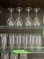 4 wine glasses and 6 drinking glasses arranged on glass shelves against a dark background.