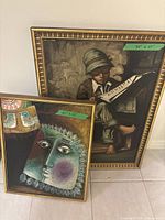 Two framed artworks leaning against wall showing size labels: larger depicts a boy reading newspaper, smaller a stylized face with birds.