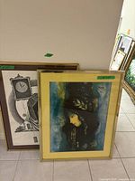 Two framed art pieces leaning against a wall, one colorful print in front and a black-and-white print at back