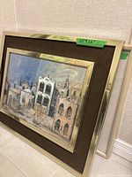 Two framed paintings leaning against a wall, showing urban scene and two figures.