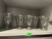 Eight clear glass ice cream mugs neatly arranged on a white shelf.