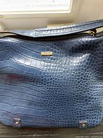 Close-up of blue faux crocodile patterned handbag with gold-tone Michael Kors label and zipper closure.