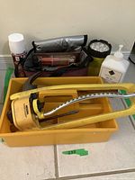 Full lot view showing yellow oscillating garden sprinkler in a yellow plastic tub with gray insulated lunch bag holding various tools, beside white pump bottle and lubricant spray can