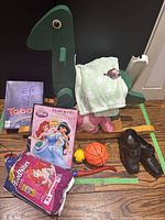 Green wooden dinosaur rocker with board games, balls, shoes, and baby diapers around it