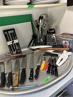 All items displayed on metal tray: knives, carving fork, honing steel, cooking utensils, cutting boards, grater, chopsticks, can opener, and boxed mini chopper
