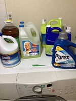 View of all detergent and cleaning supply bottles displayed on a washer top, showcasing different brands and container styles.