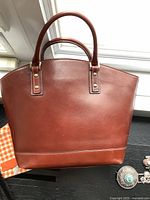 Front view of the burgundy leather handbag placed on a black surface near a window, showing overall structure and glazing of the leather.