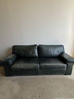 Front view of green leather sofa showing cushions and armrests, visible wear and scratches on leather