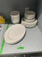 A collection of white ceramic dinnerware pieces including large oval plates, smaller plates, and bowls.