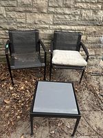 Two mesh sling chairs and matching side table positioned against stone wall