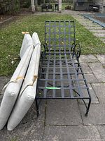 Metal lattice patio chaise lounge with curved arms beside four off-white outdoor cushions