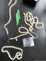 Four different pearl necklaces displayed on a black surface showing varying pearl sizes and clasps.