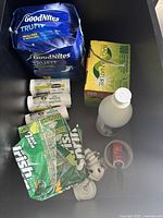 Overview of all items in the lot inside a black container including GoodNites TRU-FIT pack, biodegradable bags, white bottle, lotion tubes, and a jar with tool