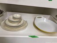 Image showing stacked plates and bowls with floral design and brown rim lines, along with an additional white handled ceramic dish