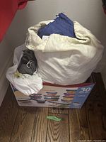 Multiple white fabric protection bags loosely stored in a box with printed label of Rubbermaid containers, some bags contents visible inside.