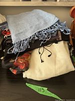 Pile of mixed scarves including light blue fringed, floral patterned, and beige textured scarves