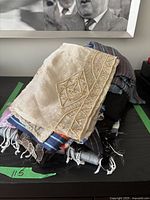 Stack of six scarves with various patterns including embroidery and stripes on a dark surface